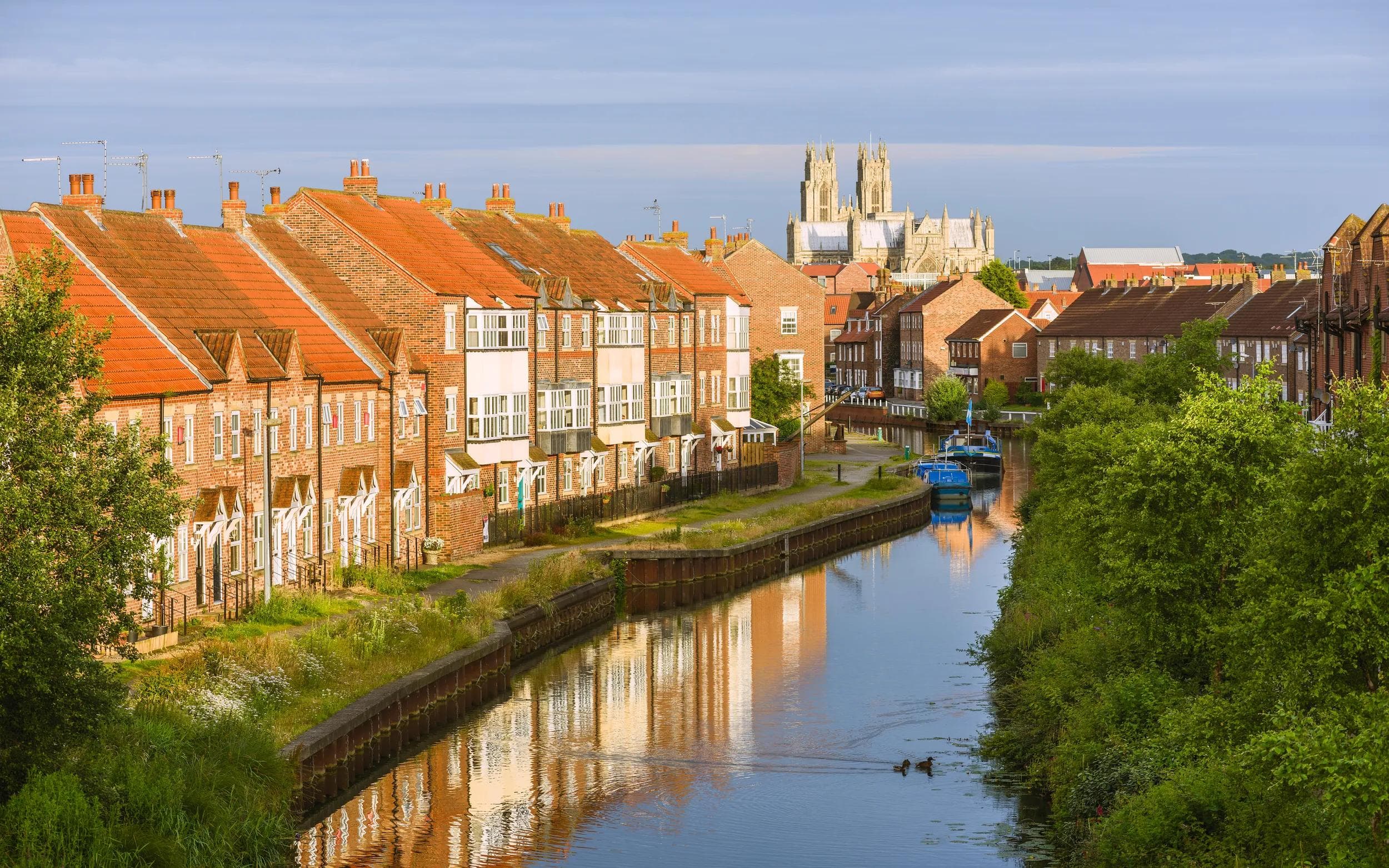 Beverley, Yorkshire, UK. The ancient minster, town houses, and the beck (canal) with barges at sunrise on a peaceful summer morning in Beverley, Yorkshire, UK.